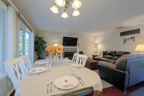 A dining area with a table set for four, a fireplace, a sofa, and a television mounted on the wall. - Lovely, Spacious Gem: Walk to Autzen & River Trail (Springfield)