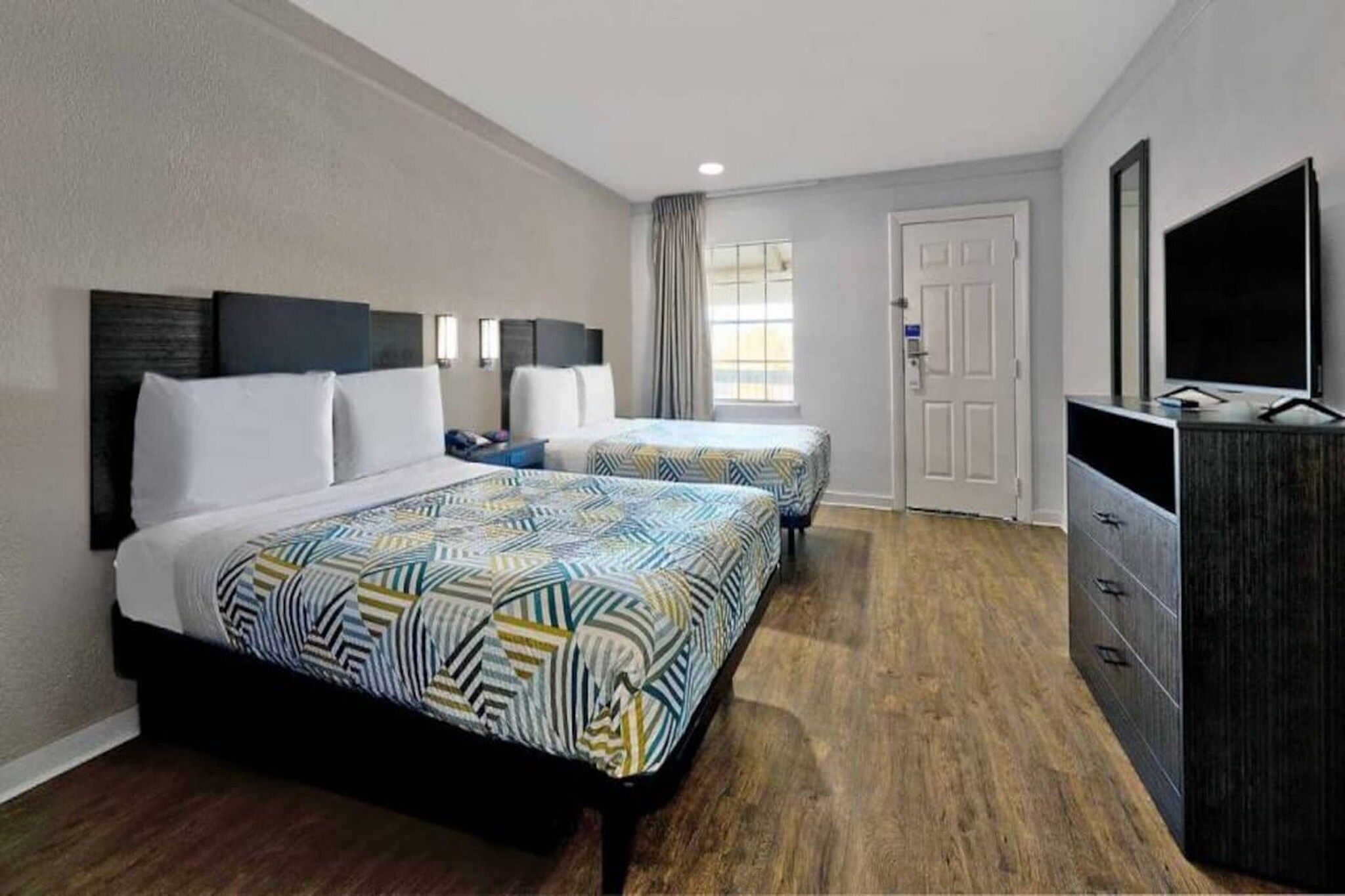 A hotel room with two beds, a TV, a dresser, and a window with curtains.