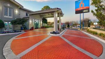 A hotel entrance with a covered walkway, a parking lot, and a billboard advertising weekly specials.