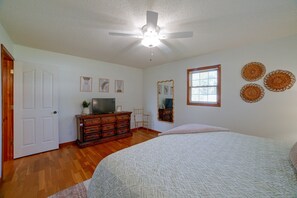 Quarto com cama, penteadeira, televisão e ventoinha no teto.