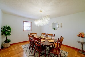 A dining room with a wooden table, chairs, a chandelier, a potted plant, and a window. - Murray Retreat w/ Game Room (Murray)