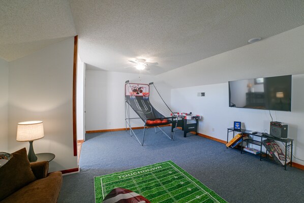 Quarto com quadra de futsal, televisão, mesa com computador e luminária.
