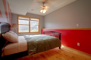 A bedroom with a bed, a window, a ceiling fan, and a red wall. - Northfield Home Near Nerstrand Big Woods (Northfield)