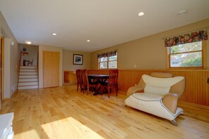Ein geräumiges Zimmer mit Holzboden, einer Essecke mit Tisch und Stühlen, einem gepolsterten Sessel und einer Treppe, die zu einer anderen Ebene führt.