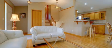 Un salon spacieux avec un canapé blanc, un escalier en bois et un coin cuisine.