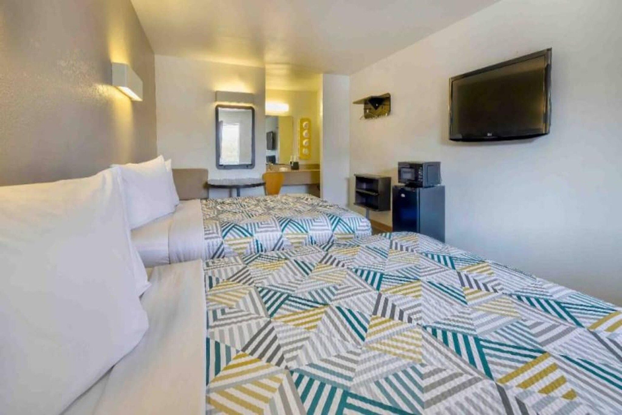 Ein Hotelzimmer mit Bett, Schreibtisch, Fernseher und Spiegel.