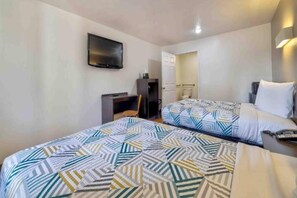 Une chambre d’hôtel avec deux lits, un bureau, une chaise, une télévision et une armoire.