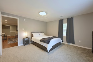 A bedroom with a bed, a bedside table, a lamp, a rug, and a view of a bathroom. - Hidden Orangeburg Gem! Spacious modern Deco Ranch (Orangeburg)