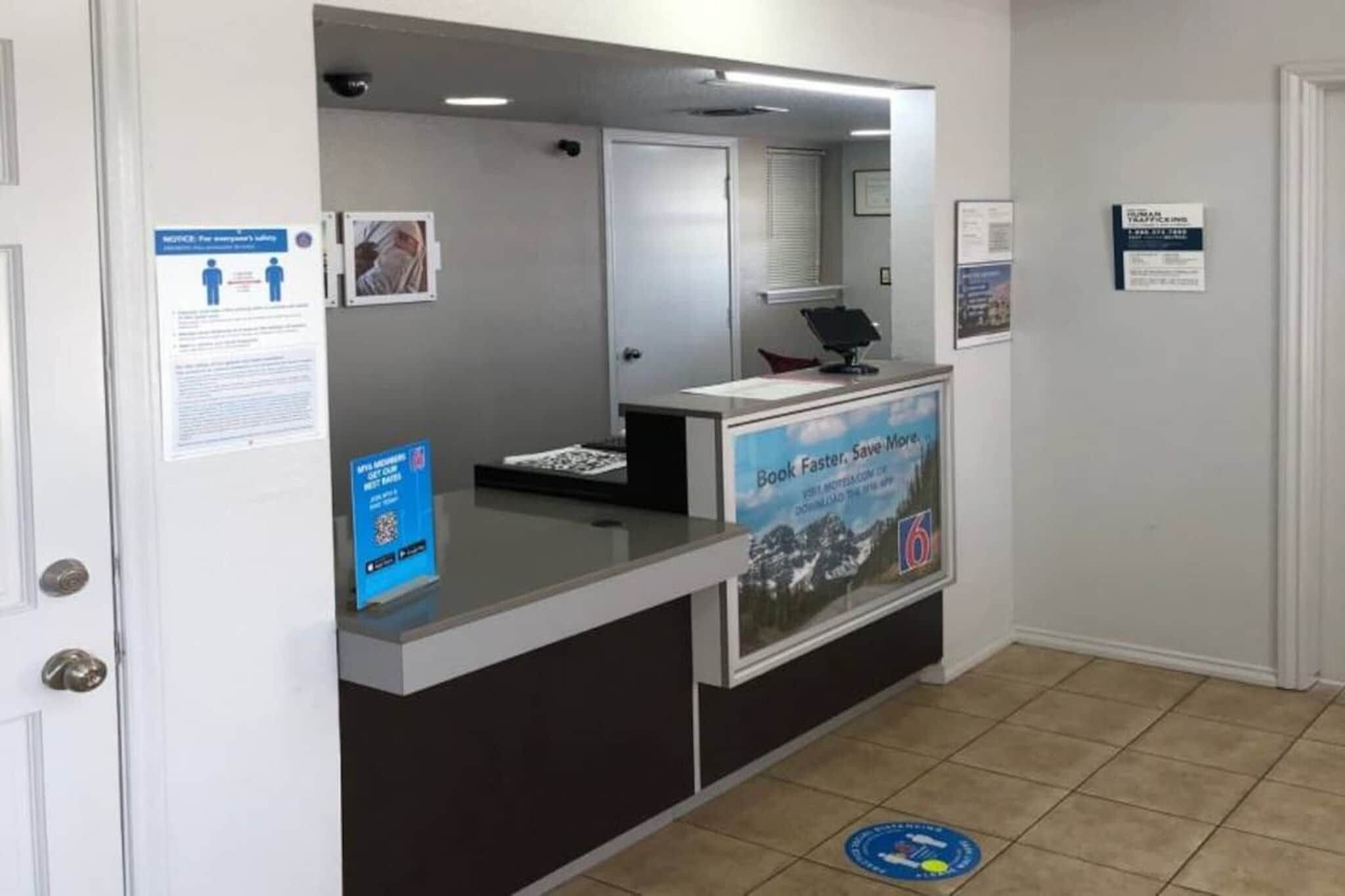 Mostrador de recepción con una computadora, un cartel que promociona un servicio más rápido y eficiente, y un letrero informativo azul.