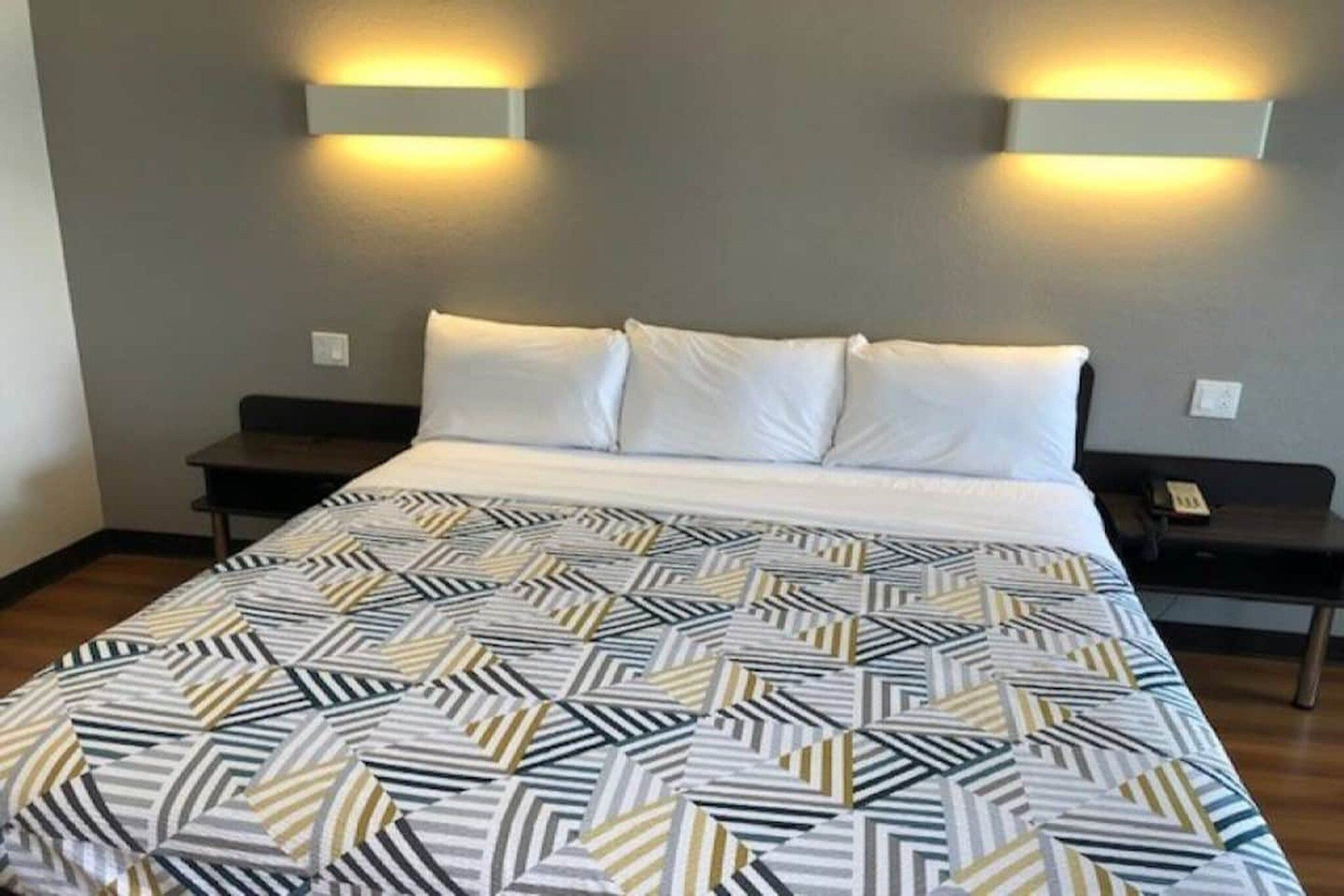 Una camera d'albergo con un letto, due comodini e illuminazione a parete.