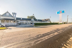 Un motel con un amplio estacionamiento, un área de estar al aire libre cubierta y un letrero visible que indica el número 6.