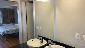 A hotel bathroom with two sinks, a mirror, and a door leading to a bedroom.