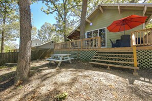 A wooden deck with a picnic table and a red umbrella, surrounded by trees and a wooden fence. - Fishing Cabin on Lake Bob Sandlin (Leesburg)