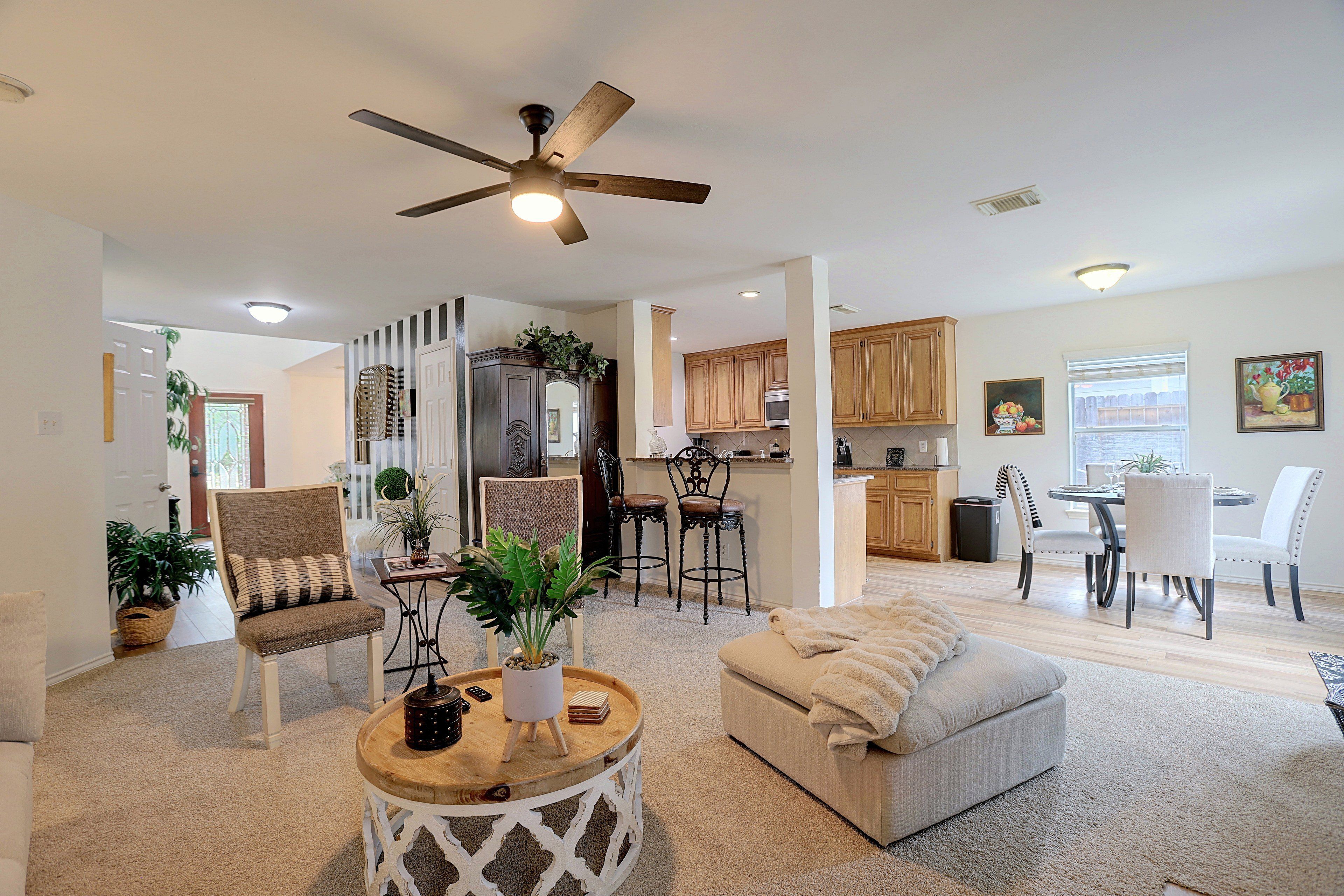A spacious living room with a ceiling fan, a dining area with a table and chairs, and a kitchen with wooden cabinets.