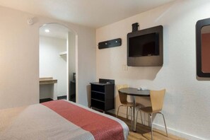 A hotel room with a bed, a desk with a chair, a television mounted on the wall, and a small table. - 1 King Bed | Smoking, Micfridge (Fort Worth)