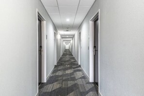 Un largo pasillo estrecho con piso alfombrado y paredes blancas, que conduce a varias puertas a ambos lados.