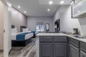 Habitación de hotel moderna con una cama grande, zona de estar separada, kitchenette y vista a la ciudad.