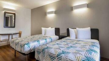 A hotel room with two beds, a small table, and a mirror.