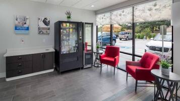 A reception area with a counter, a refrigerator, two red chairs, and large windows with a view of parked cars outside.