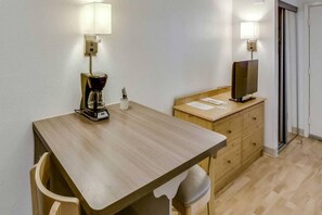 A small, simple room with a wooden table, a coffee maker, a television on a wooden cabinet, and a door. - 1 Queen Bed | ADA/Tub, Nsmk (Houston)