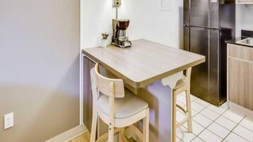 A small kitchen with a wooden table, two chairs, a coffee maker, and a stainless steel refrigerator.