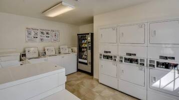 A laundry room with multiple washing machines and dryers, a refrigerator, and a tiled floor.