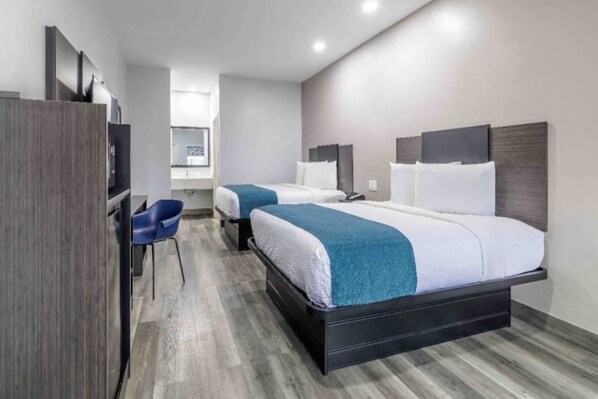 A hotel room with two beds, a desk, and a chair.