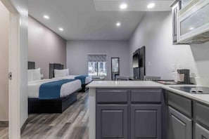 A modern hotel room with a large bed, a kitchenette, and a bathroom.