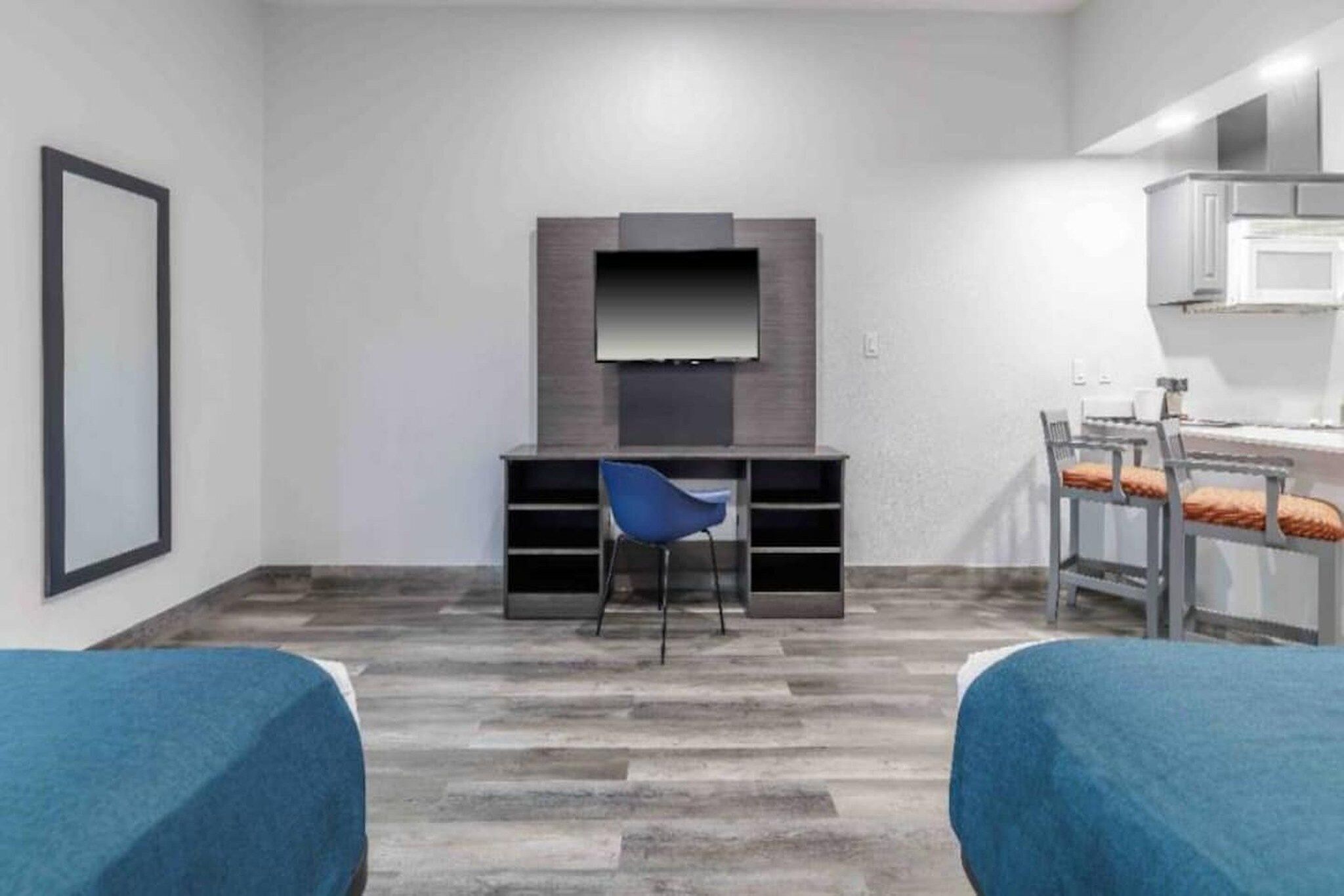 A modern room with a flat-screen TV mounted on the wall, a blue chair, a desk with a chair, and two beds with blue bedding.