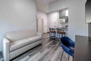 A modern living room with a sofa, a dining area with chairs, and a kitchen area with a microwave.