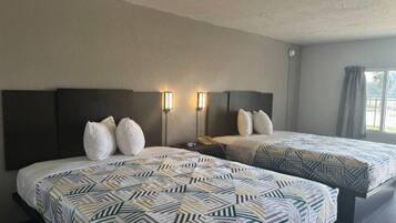 A hotel room with two beds, each with patterned bedding and headboards, a nightstand, and wall-mounted reading lamps.