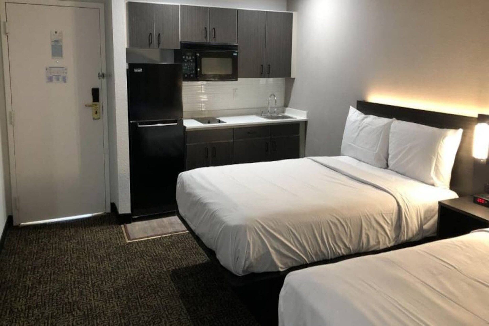 Una habitación de hotel con cama, mesita de noche, lámpara, microondas y refrigerador.