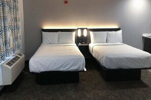 A hotel room with two single beds, a bedside table with a lamp, a heater, and a patterned curtain. - 2 Full Beds | Non-Smoking, Kitchen (Killeen TX)