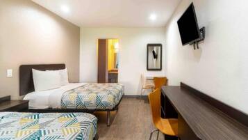 Habitación de hotel con dos camas, un escritorio, una silla, un televisor y una puerta que da a otra habitación.