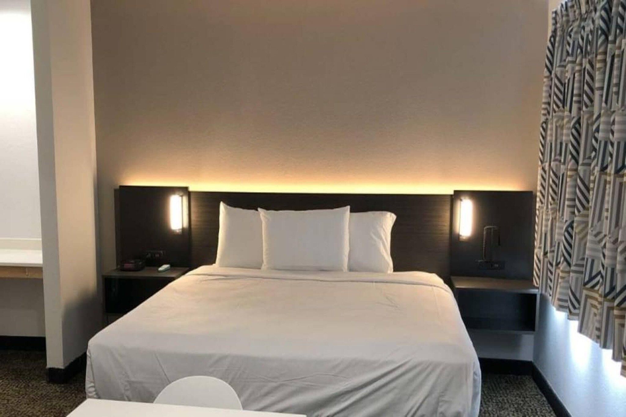 Quarto de hotel com uma cama grande, duas mesas de cabeceira, um criado-mudo e uma cadeira.