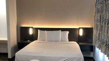 Quarto de hotel com uma cama grande, duas mesas de cabeceira, um criado-mudo e uma cadeira.