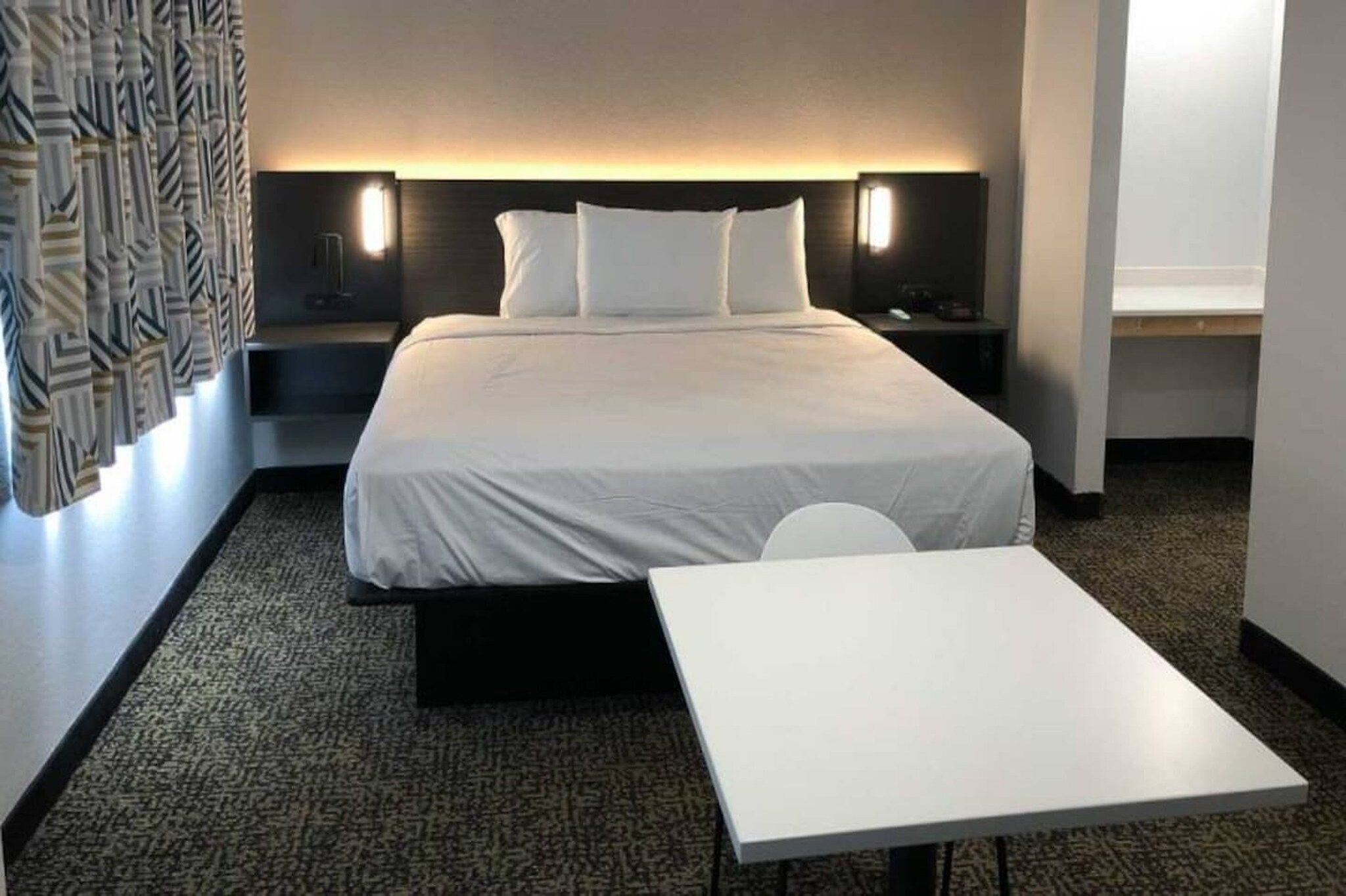 A hotel room with a bed, bedside tables, a desk, and a patterned curtain.