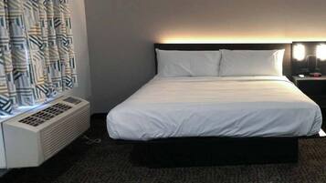 Quarto de hotel com cama, aquecedor, mesa de cabeceira com abajur e cortina estampada.