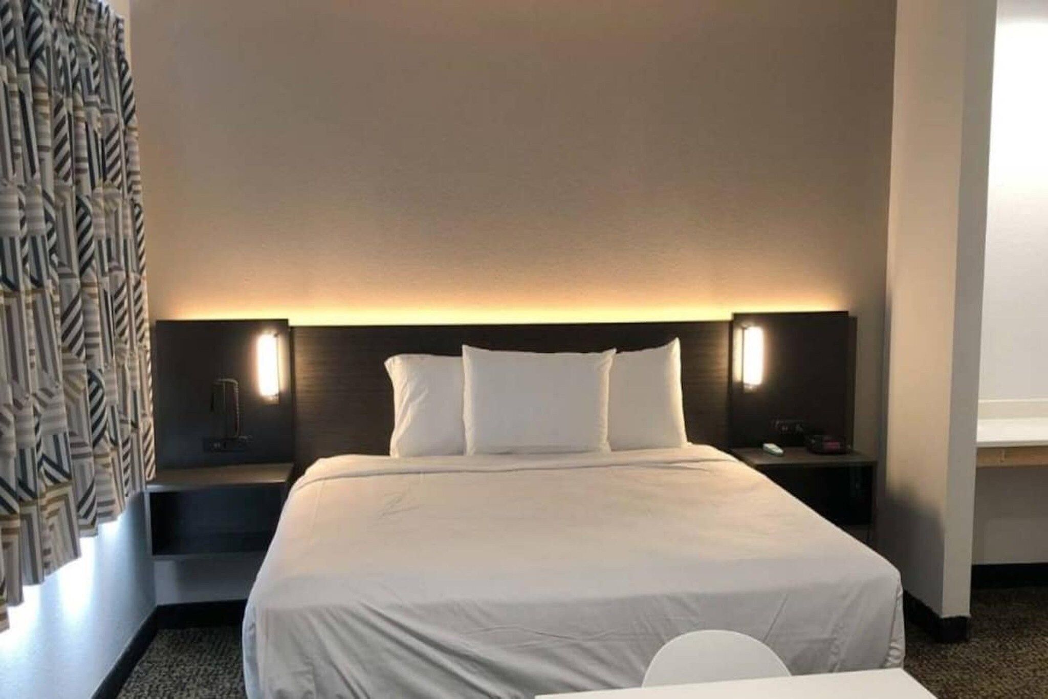 A hotel room with a large bed, two bedside tables, and a headboard with integrated lighting.