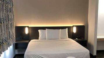 A hotel room with a large bed, two bedside tables, and a headboard with integrated lighting.