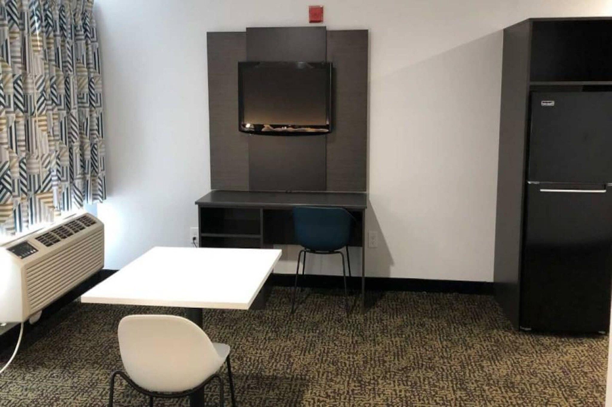 A small room with a white table, a blue chair, a black cabinet, and a television mounted on the wall.