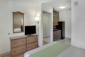 A hotel room with a bed, a dresser, a television, a mirror, a door, and a kitchenette. - 1 Queen Bed | Micfridge, Smoking (Stafford)