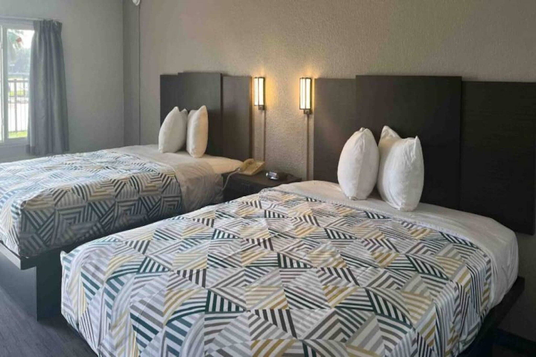 Ein Hotelzimmer mit zwei Betten, jeweils mit gemusterten Laken, einem Nachttisch mit Telefon und Wandleuchten.