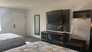 A hotel room with two beds, a desk, a chair, a television, and a door.