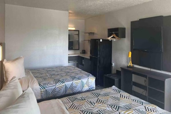 Une chambre d’hôtel avec deux lits, une télévision, un réfrigérateur et un petit bureau.