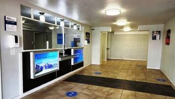 A hotel lobby with a reception desk, a digital screen displaying a cityscape, and a tiled floor with directional markers.