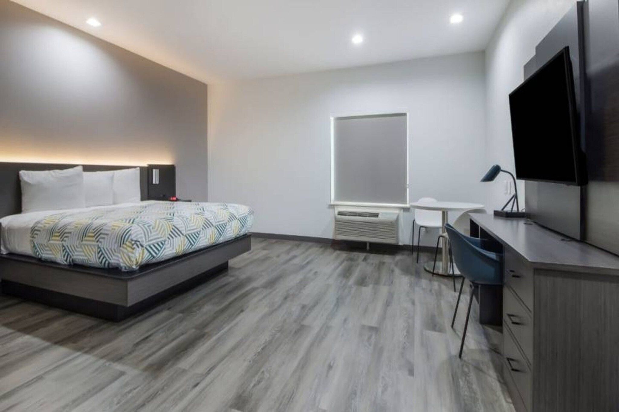 Una habitación de hotel moderna con cama, escritorio, silla, televisor y un ventanal grande.