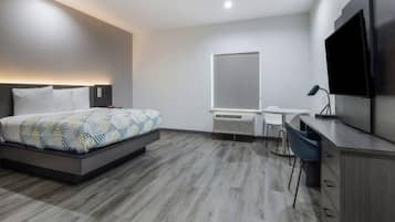 Una habitación de hotel moderna con cama, escritorio, silla, televisor y un ventanal grande.