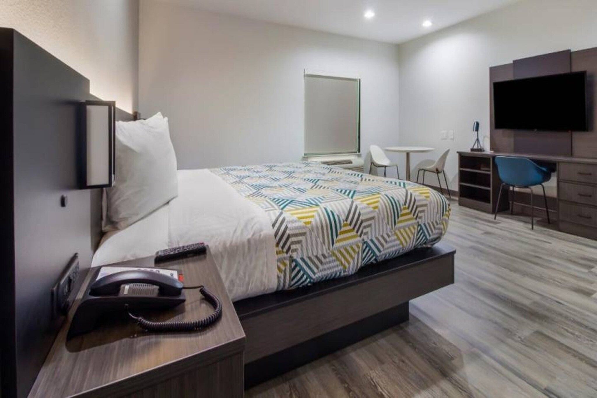Una habitación de hotel moderna con cama, mesita de noche, escritorio, silla y televisor.