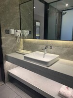 Un baño moderno con un espejo grande, un lavamanos blanco y una ducha empotrada.